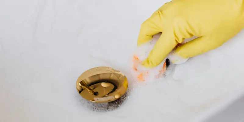 A gloved hand cleaning around a sink drain