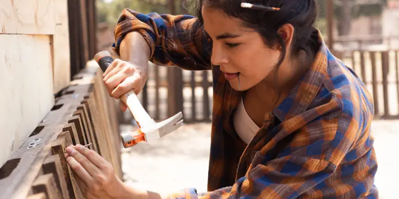 A woman hammering a fence board into place