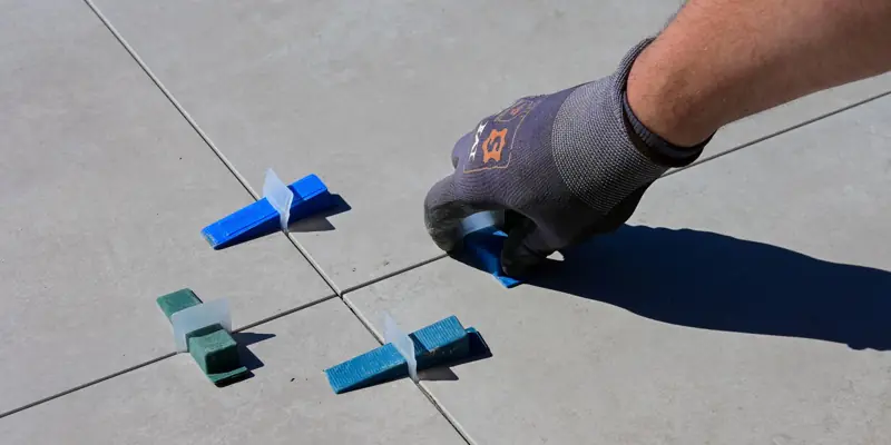 A gloved hand setting floor tile with spacers